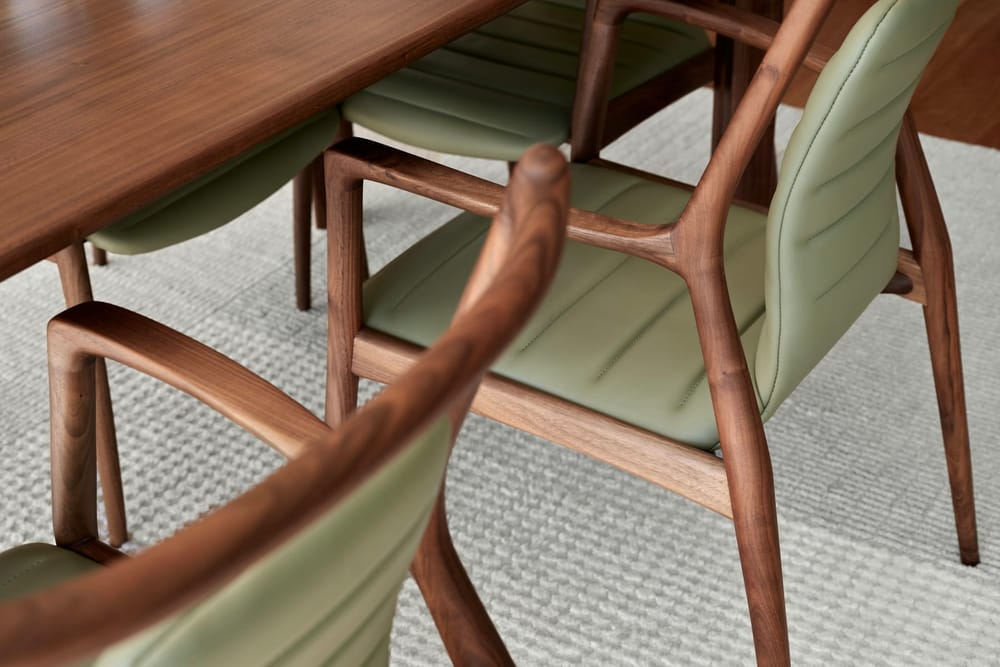 Houten eetkamerstoelen met armleuningen en groene zittingen aan een houten tafel