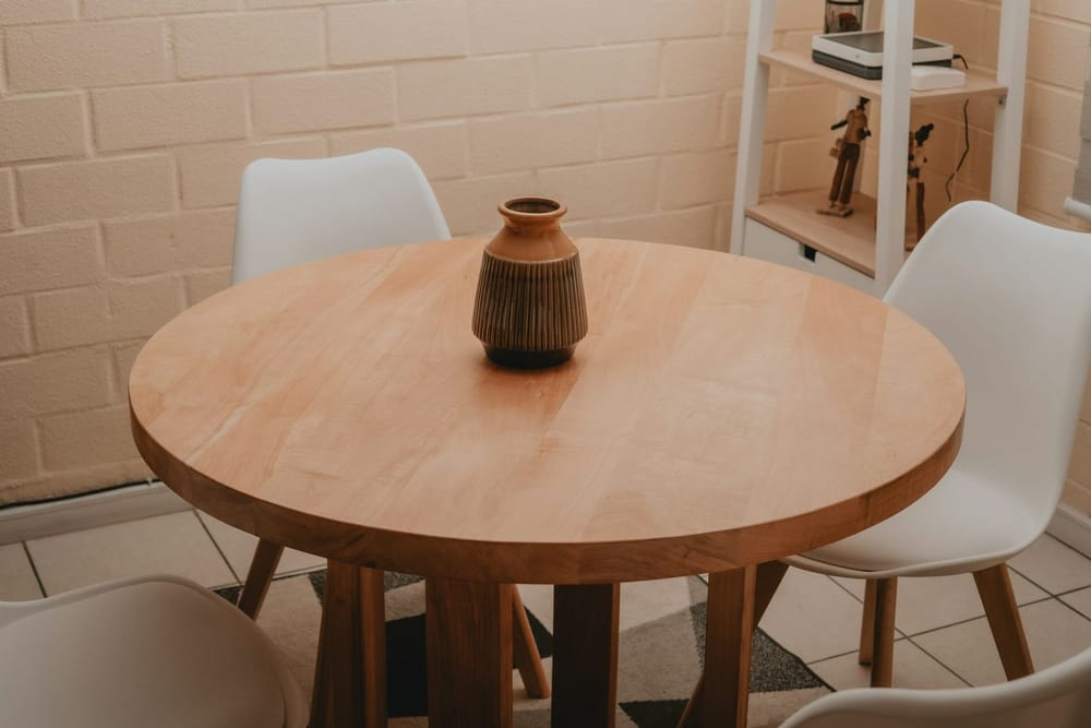 Een ronde houten tafel met een vaas in het midden en witte stoelen eromheen