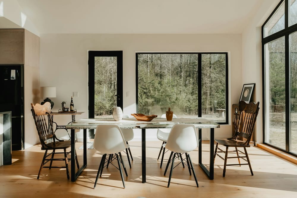 Zwarte stalen frames onder een tafel met een licht blad, met witte kuipstoelen voor grote ramen